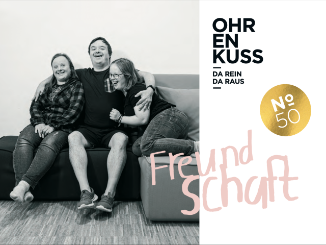 Das Cover der aktuellen Ohrenkuss-Ausgabe. Auf dem Cover sieht man ein schwarz-weiß-Foto von 3 Personen mit Down-Syndrom auf einer Couch. Ein Mann sitzt lächelnd in der Mitte und hält die beiden Frauen im Arm.