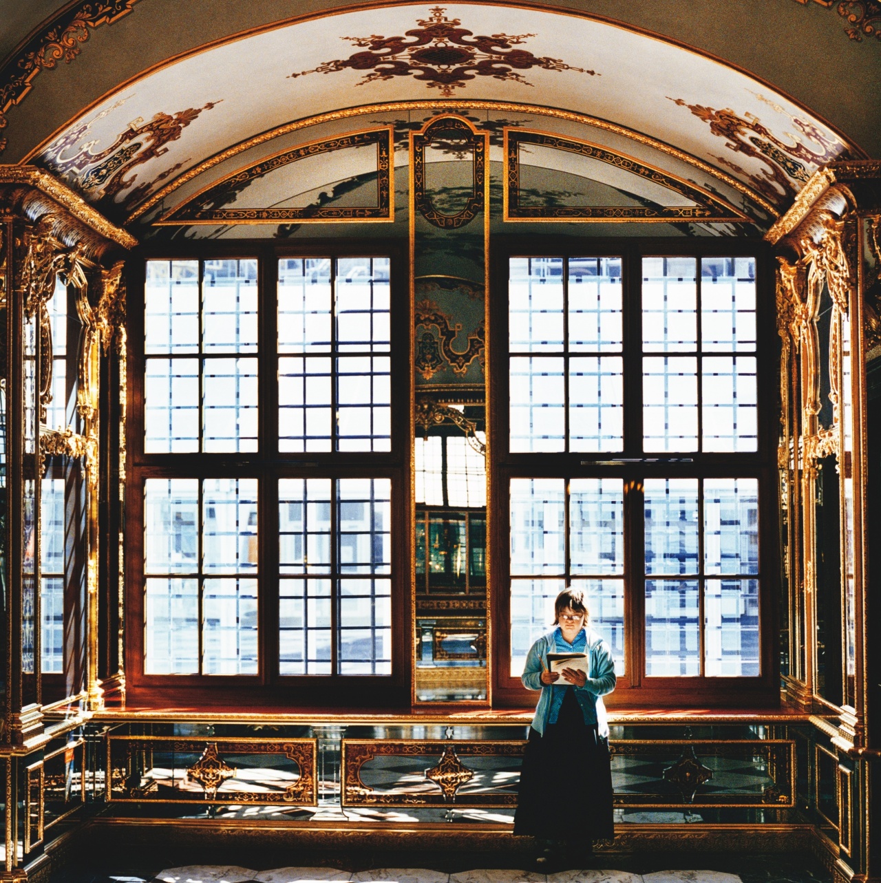 Christinae Grieb steht im Juwelenzimmer, Historisches Grünes Gewölbe, Staatliche Kunstsammlungen Dresden und liest. Das helle Licht, das durch die Fenster scheint, lässt den Fußboden funkeln