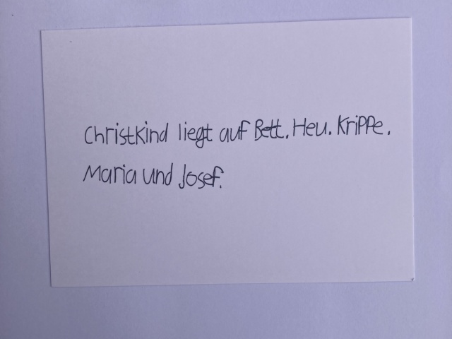 Handschriftlicher Schriftzug: Christkind liegt auf Bett. Heu. Krippe. Maria und Josef.